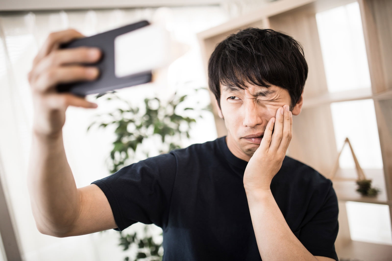 虫歯で頬を押さえながらスマートフォンで自撮りする男性［モデル：大川竜弥］