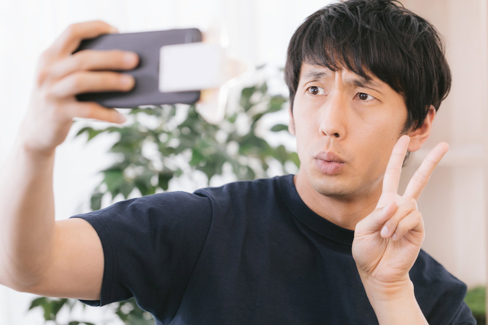 スマートフォンで自撮りをしながらピースサインをする男性［モデル：大川竜弥］