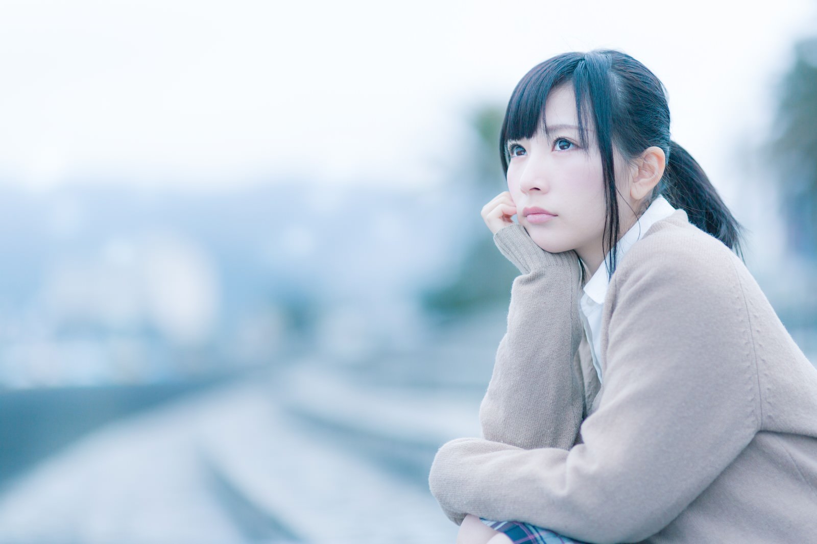 屋外で座り込み、物思いにふける女子高生の表情を捉えた写真［モデル：モデルリリース］