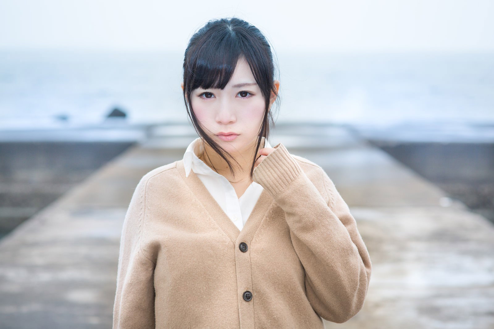 ベージュのカーディガンを着た女子高生が寂れた埠頭で海を眺めている［モデル：モデルリリース］