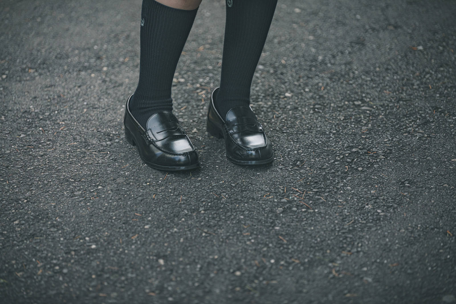 黒いローファーと紺色のハイソックスを履いた学生の足元［モデル：石投げて美奈代］