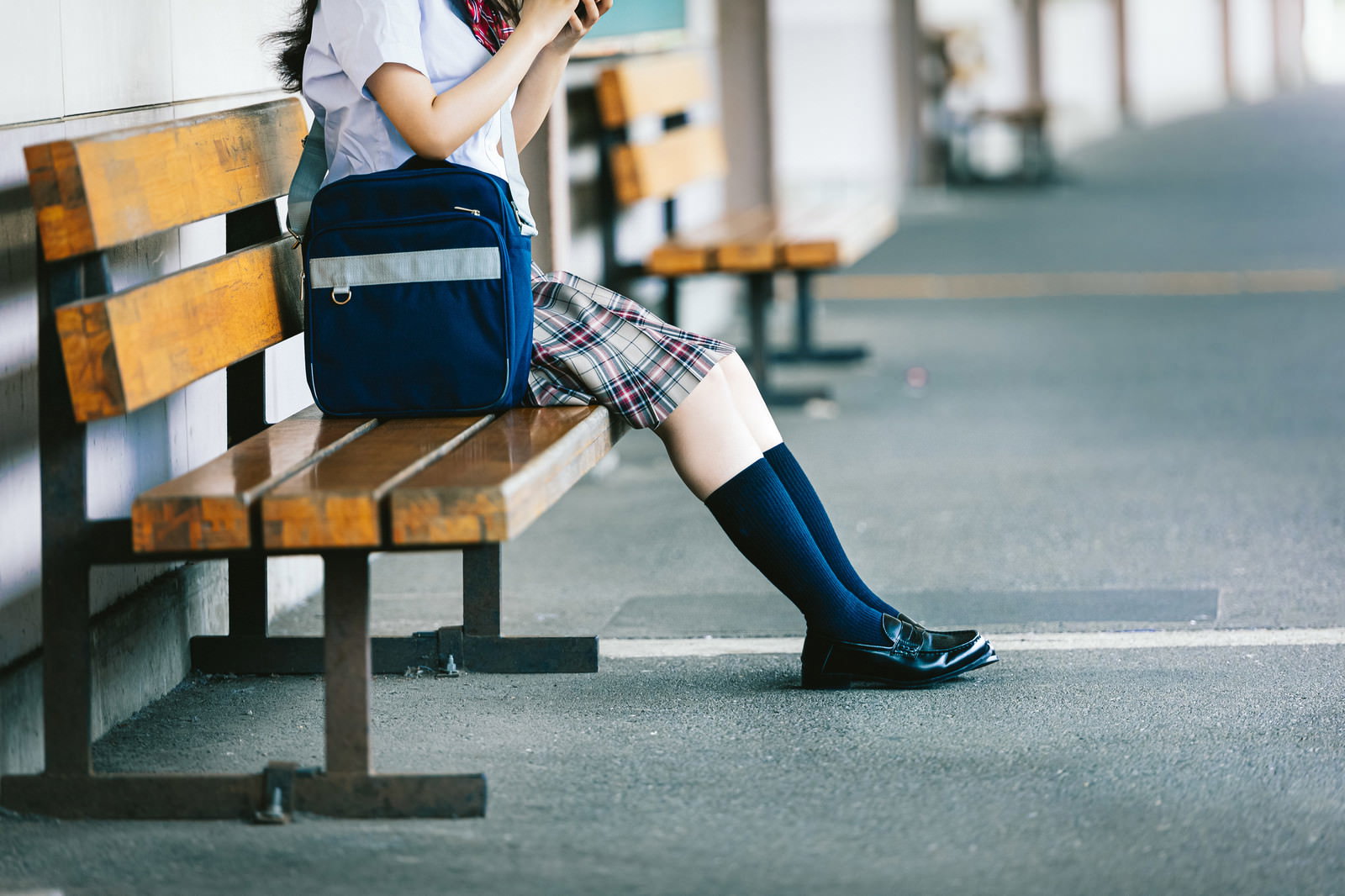 制服を着た女子高生が駅のホームのベンチに座っている［モデル：石投げて美奈代］