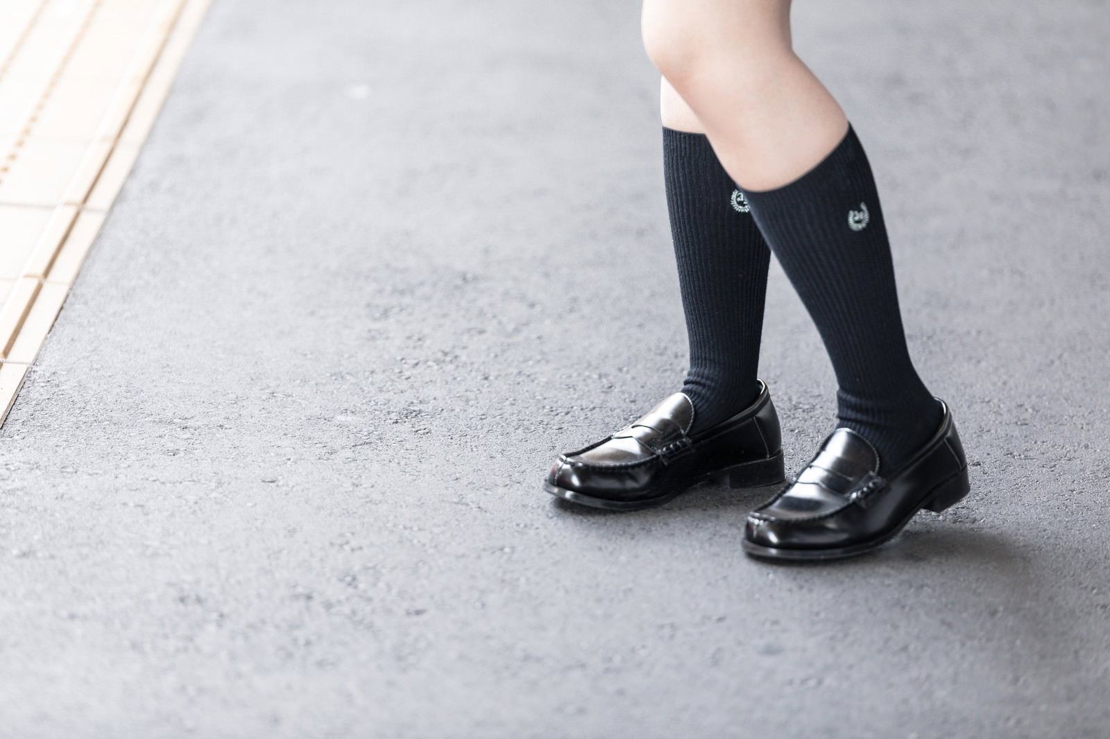 黒いローファーと紺色のハイソックスを履いた女子高生の足元［モデル：石投げて美奈代］