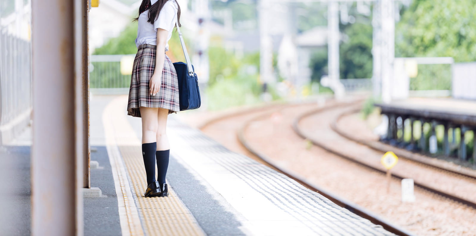 誰もいない田舎の駅のホームで振り返る制服姿の女子高生［モデル：石投げて美奈代］
