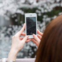 スマホのカメラを桜の花に近づけて撮影する女性の手元の写真