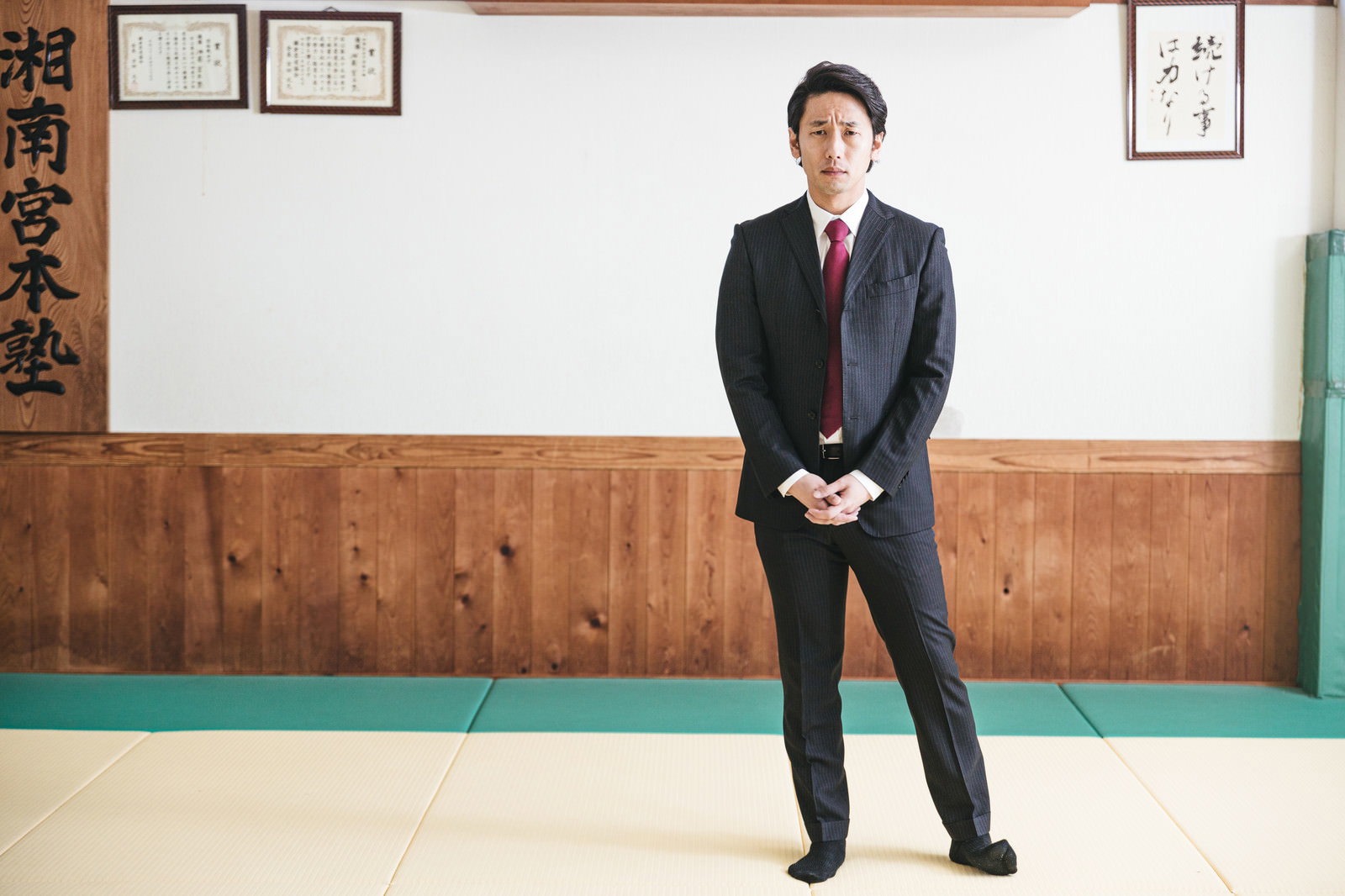 柔道場の畳の上に黒いスーツを着て立っている男性［モデル：大川竜弥］