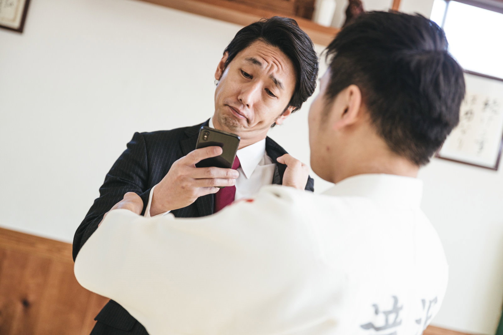 白い柔道着を着た男性が組み手中にスマートフォンを見ている［モデル：大川竜弥］