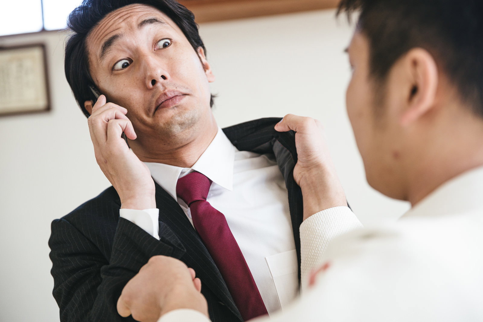 電話中に後ろから襟を掴まれる赤いネクタイのスーツ男性［モデル：大川竜弥］