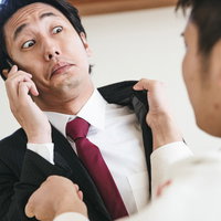 もしもし？私いま襲われてます。電話中に後ろから襉を掴まれるスーツ男性の写真