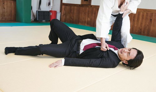 道場で柔道の投げ技に倒されるスーツ姿のビジネスマン