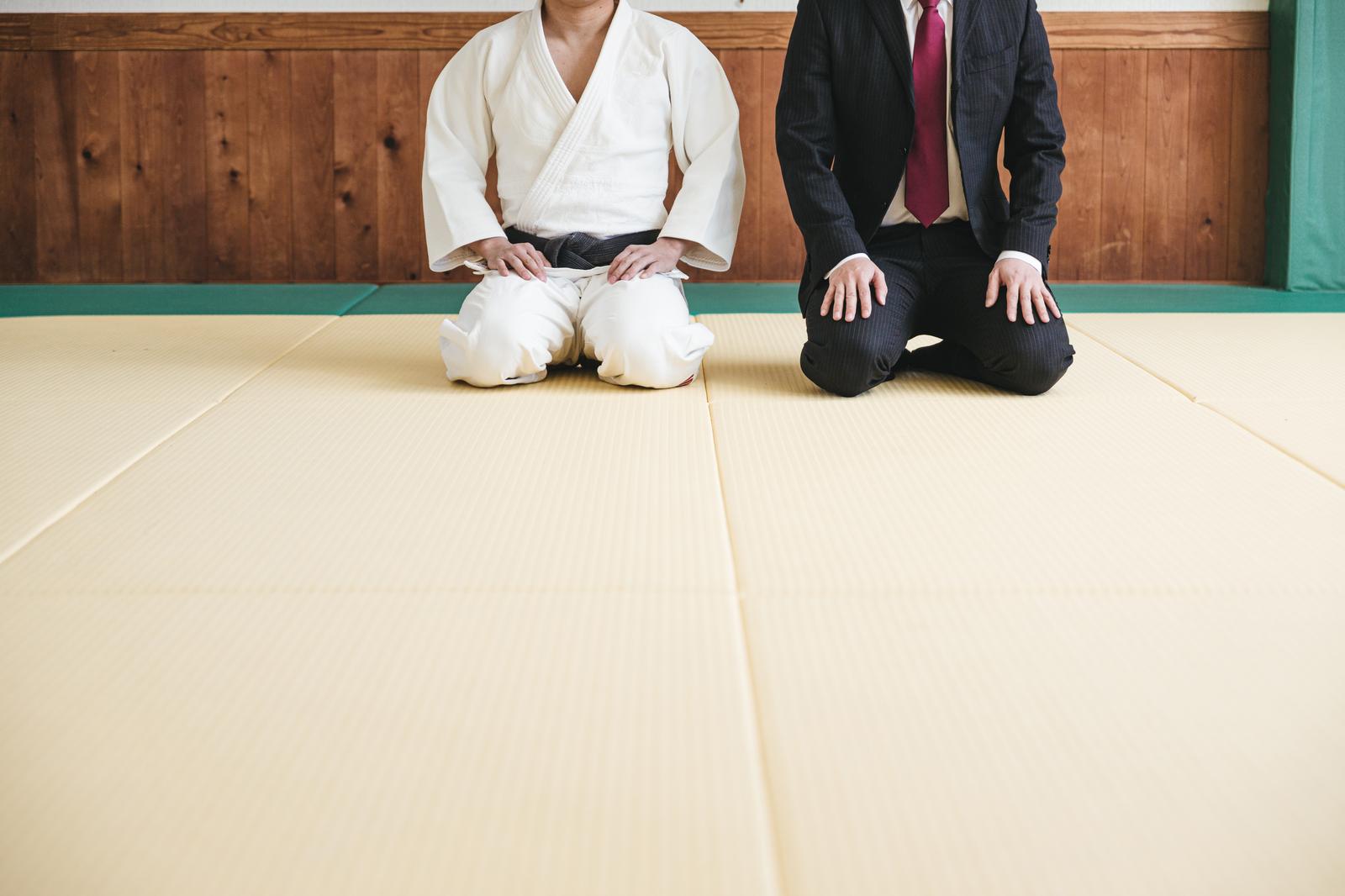 畳の上で正座する柔道着の男性とスーツ姿の男性が並んでいる様子［モデル：大川竜弥］