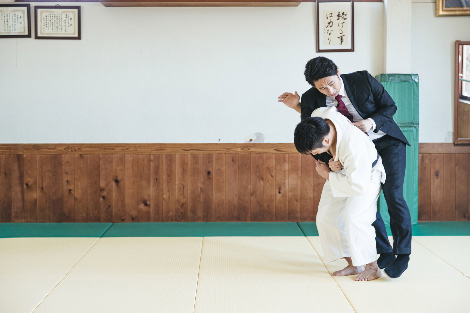 道場で一本背負いの投げ技をかけられるスーツ姿の男性［モデル：大川竜弥］