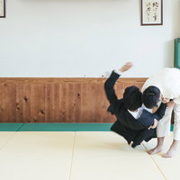 白い柔道着で一本背負いを決める、スーツ姿のサラリーマンの写真