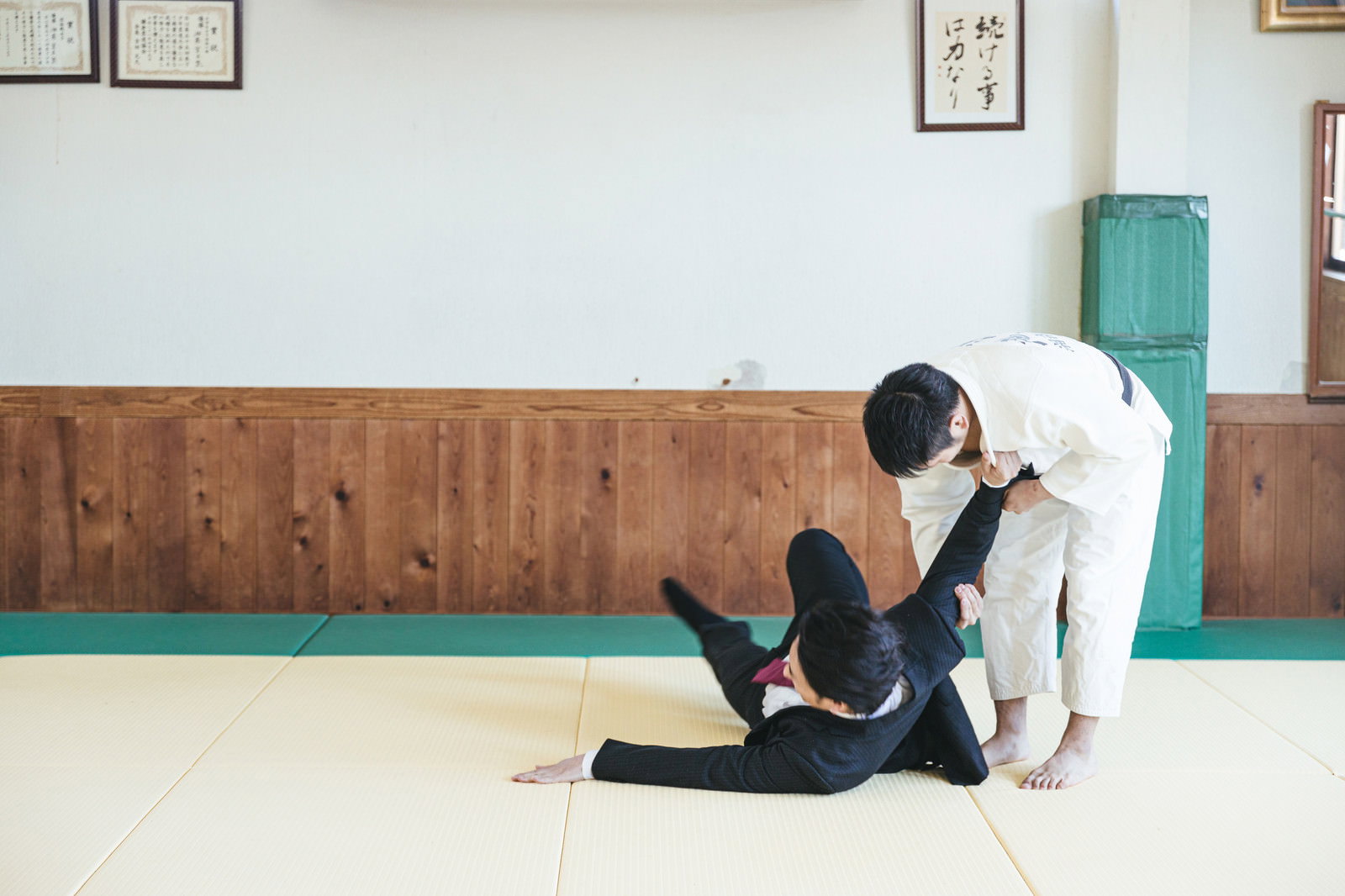 道場で柔道着の人物がスーツ姿のサラリーマンを一本背負いで投げている［モデル：大川竜弥］
