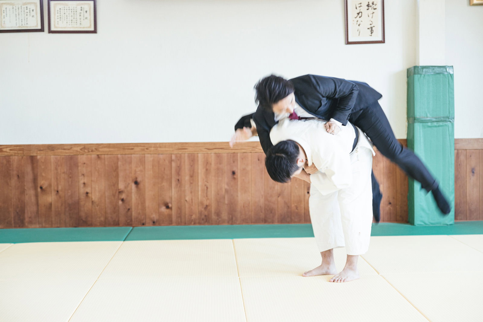 道場で一本背負いによって豪快に投げられるスーツ姿の会社員男性［モデル：大川竜弥］