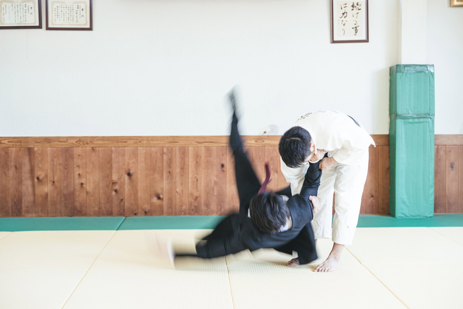畳の上で一本背負いを決められるスーツ姿の会社員男性［モデル：大川竜弥］