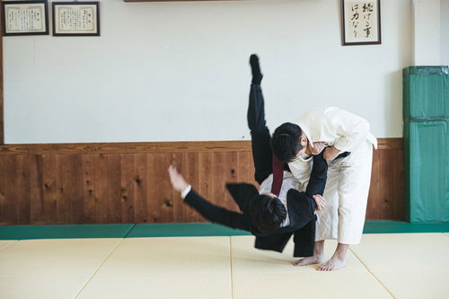 道場で繰り出す一本背負い、柔道着とスーツ姿の男性