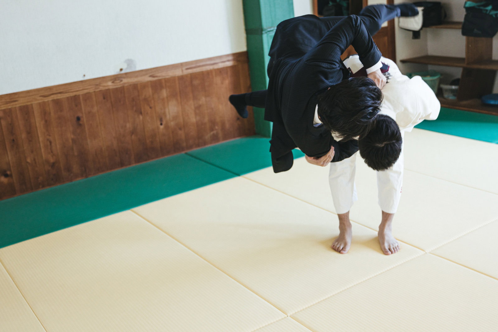 柔道着とスーツの男性が畳の上で一本背負いを決める瞬間［モデル：大川竜弥］