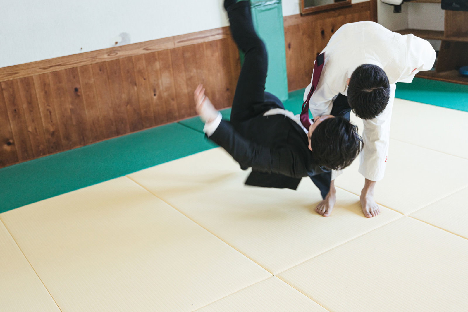 道場でスーツ姿の男性を一本背負いで投げ飛ばす白い柔道着の男性［モデル：大川竜弥］