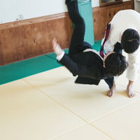 白い柔道着の男性がスーツ姿の男性を一本背負いで投げ飛ばすの写真