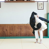 柔道場でサラリーマンを投げ技で倒す男性の格闘技スポーツの写真