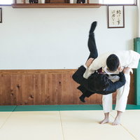 柔道場でサラリーマンを投げる白い柔道着の男性の写真