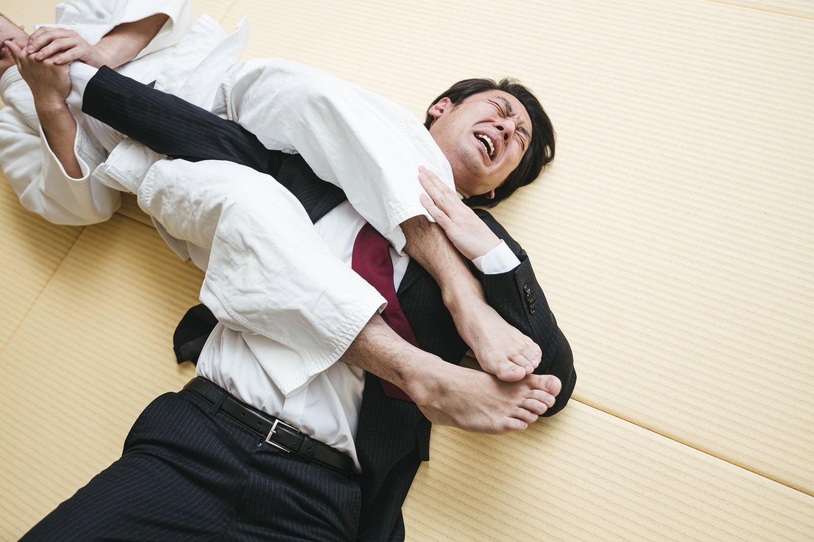 道場で腕ひしぎ十字固めをかけられギブアップする白いスーツ姿の男性［モデル：大川竜弥］
