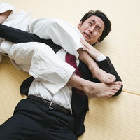 罰ゲームで右腕の関節を決められて悶えるスーツ姿の男性の写真