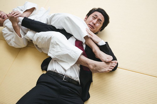 罰ゲームで右腕の関節を決められて悶えるスーツ姿の男性