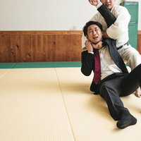 必死に片羽絞めから逃れようとするスーツ姿の会社員の写真