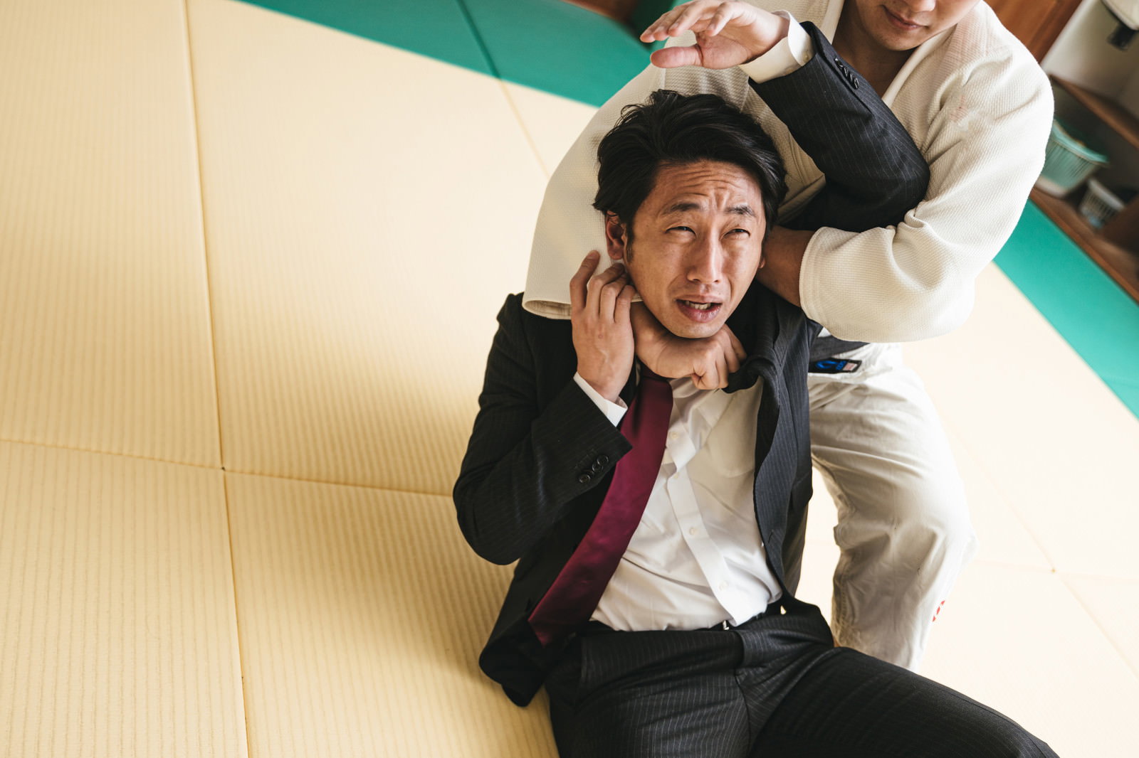 道場の畳で片羽絞めをかけられるスーツ姿の男性［モデル：大川竜弥］