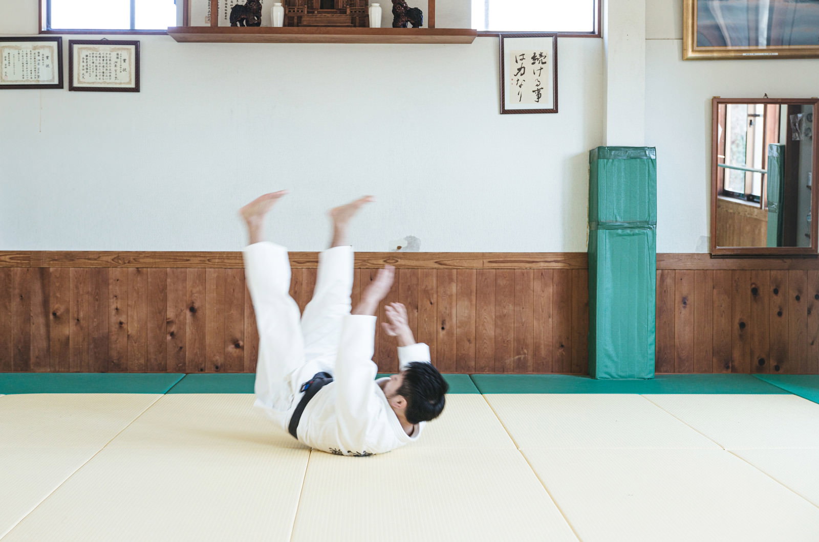 柔道場の畳の上で前回り受け身を行う白い道着の男性
