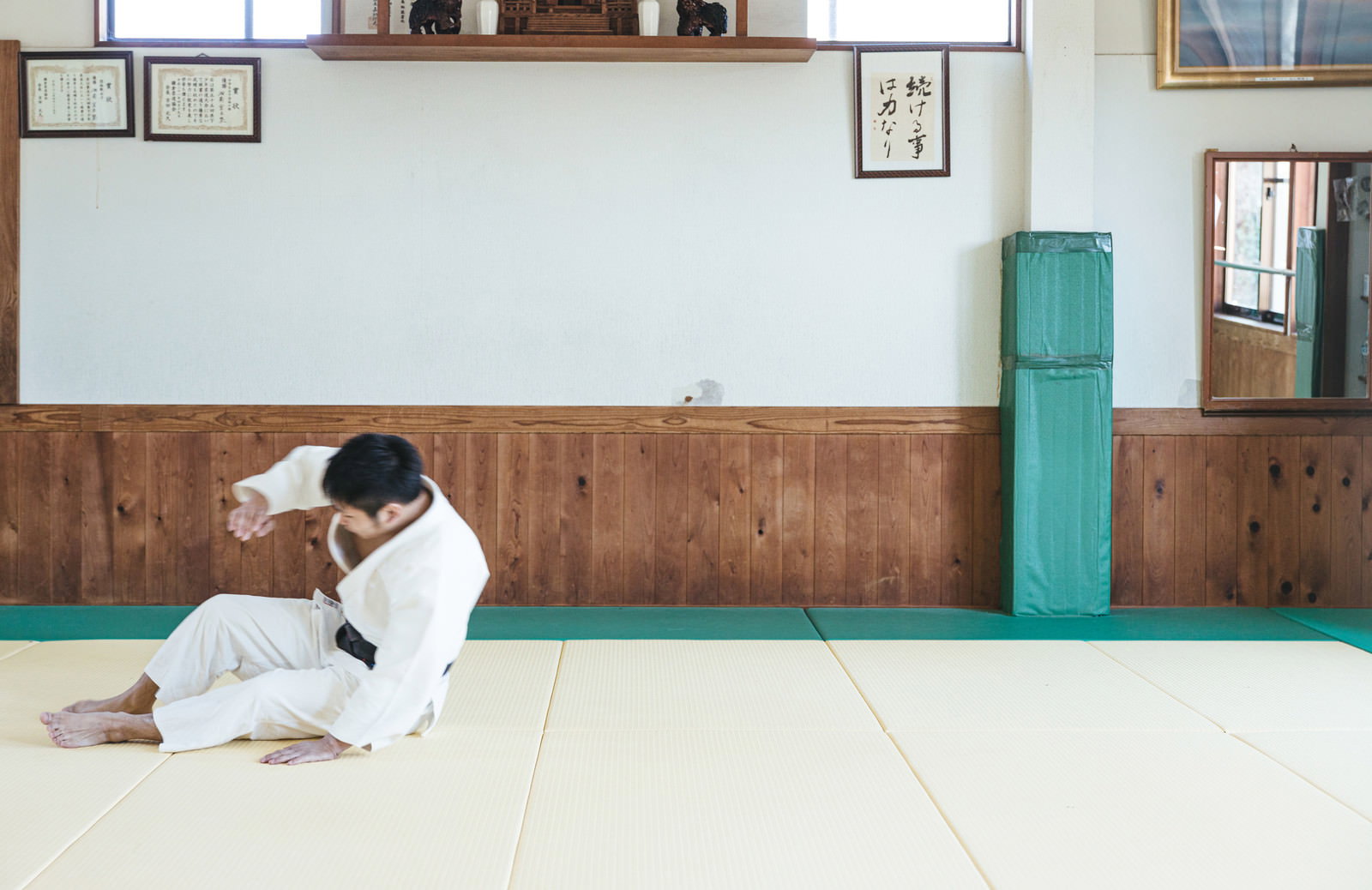 畳の上で前回り受け身を行う白い道着を着た男性の柔道練習シーン