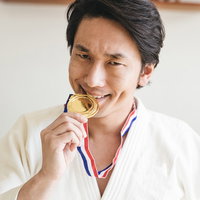 金メダルを噛む柔道選手の優勝喜びを表現した道着姿の男性の写真