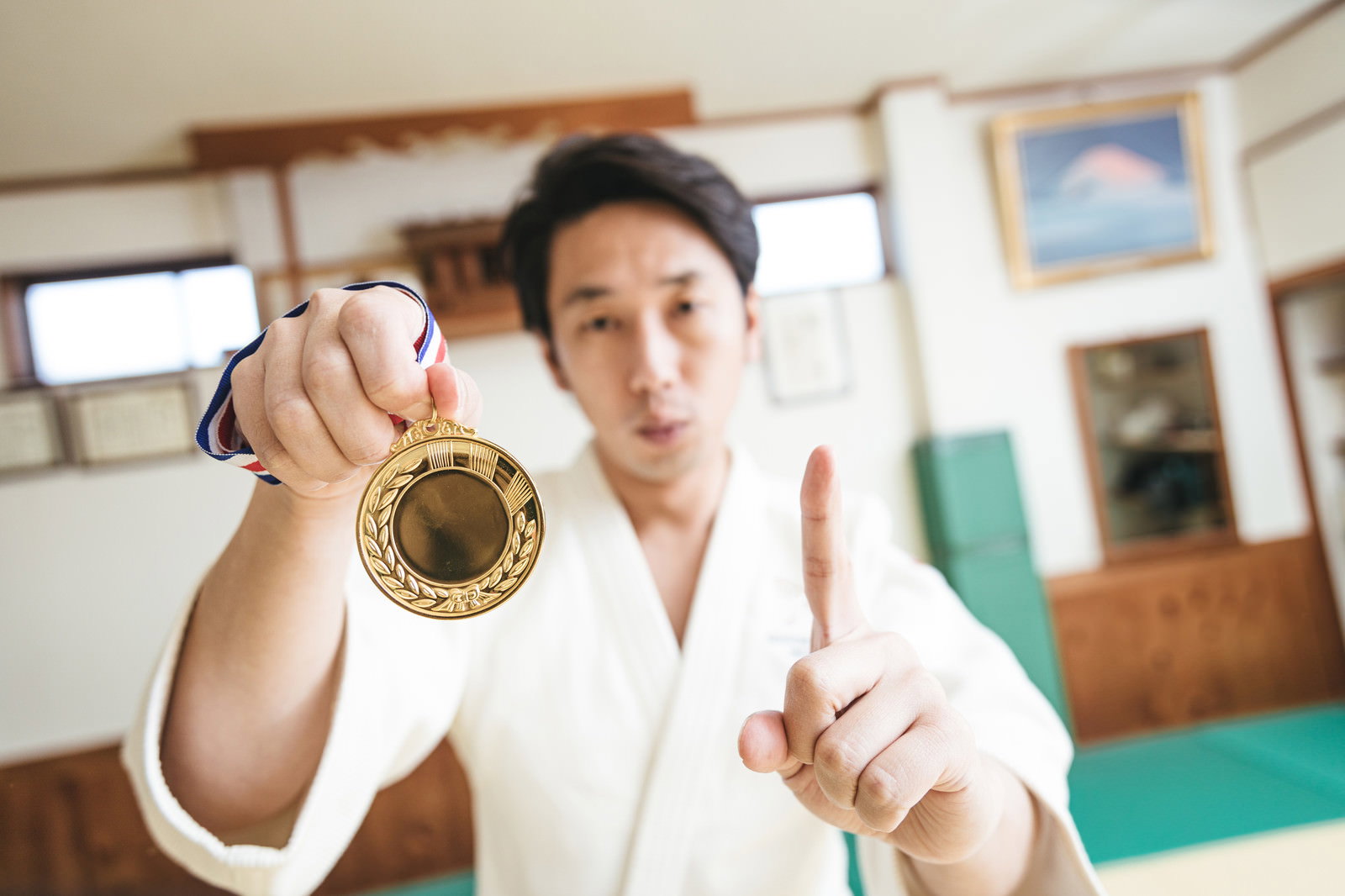 金メダルを持ちピースサインをする白い道着姿の男性［モデル：大川竜弥］