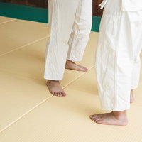 柔道の組手をしている選手たちの足元と道着、畳での稽古風景の写真