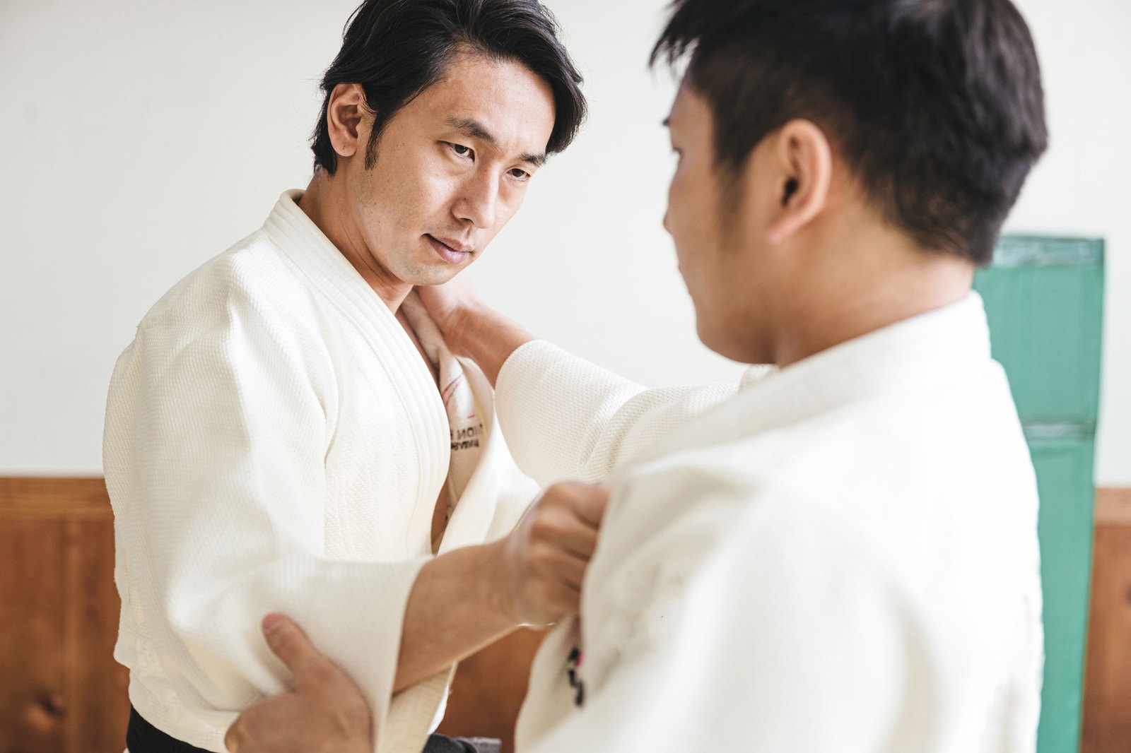 畳の上で白い道着を着た2人の男性が組み手を取る柔道試合［モデル：大川竜弥］