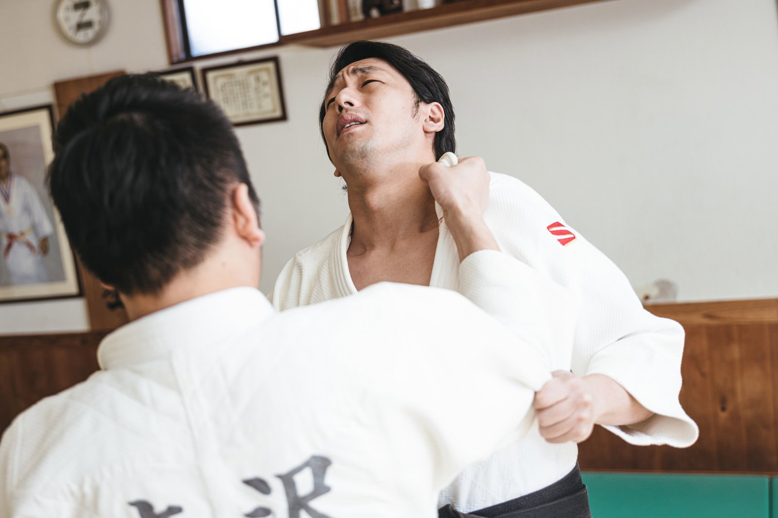 畳の上で白い道着を着た2人の男性が柔道の組み手を練習している［モデル：大川竜弥］