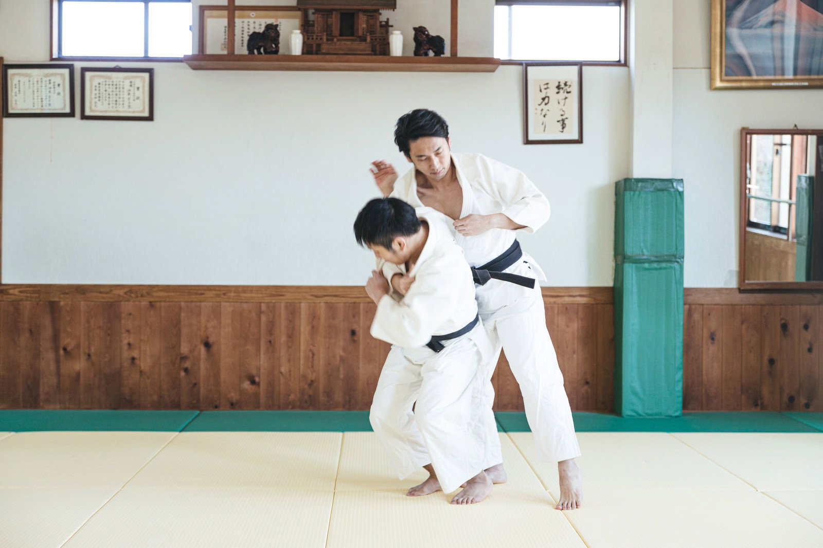道場の畳の上で柔道の一本背負いを決める白い柔道着の男性［モデル：大川竜弥］