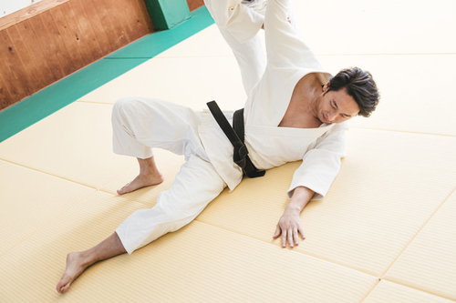 白い柔道着で畳の上に受け身をとる男性の基本動作