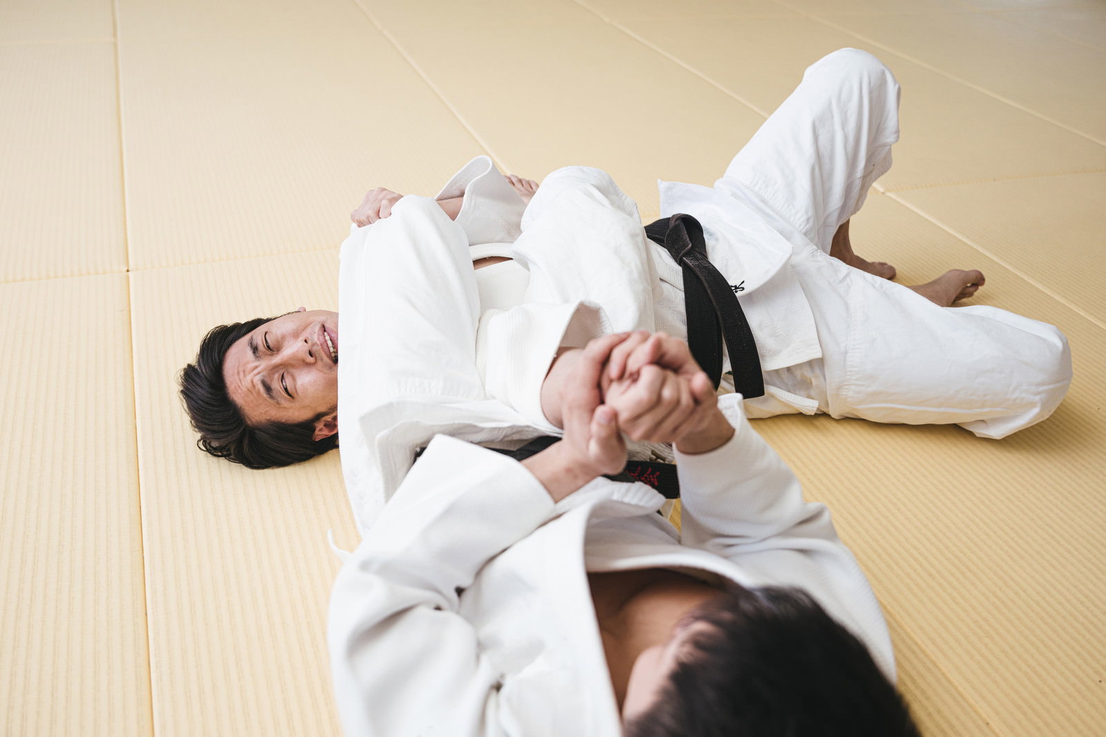 畳の上で腕ひしぎ十字固めを決める白い柔道着姿の男性柔道選手［モデル：大川竜弥］