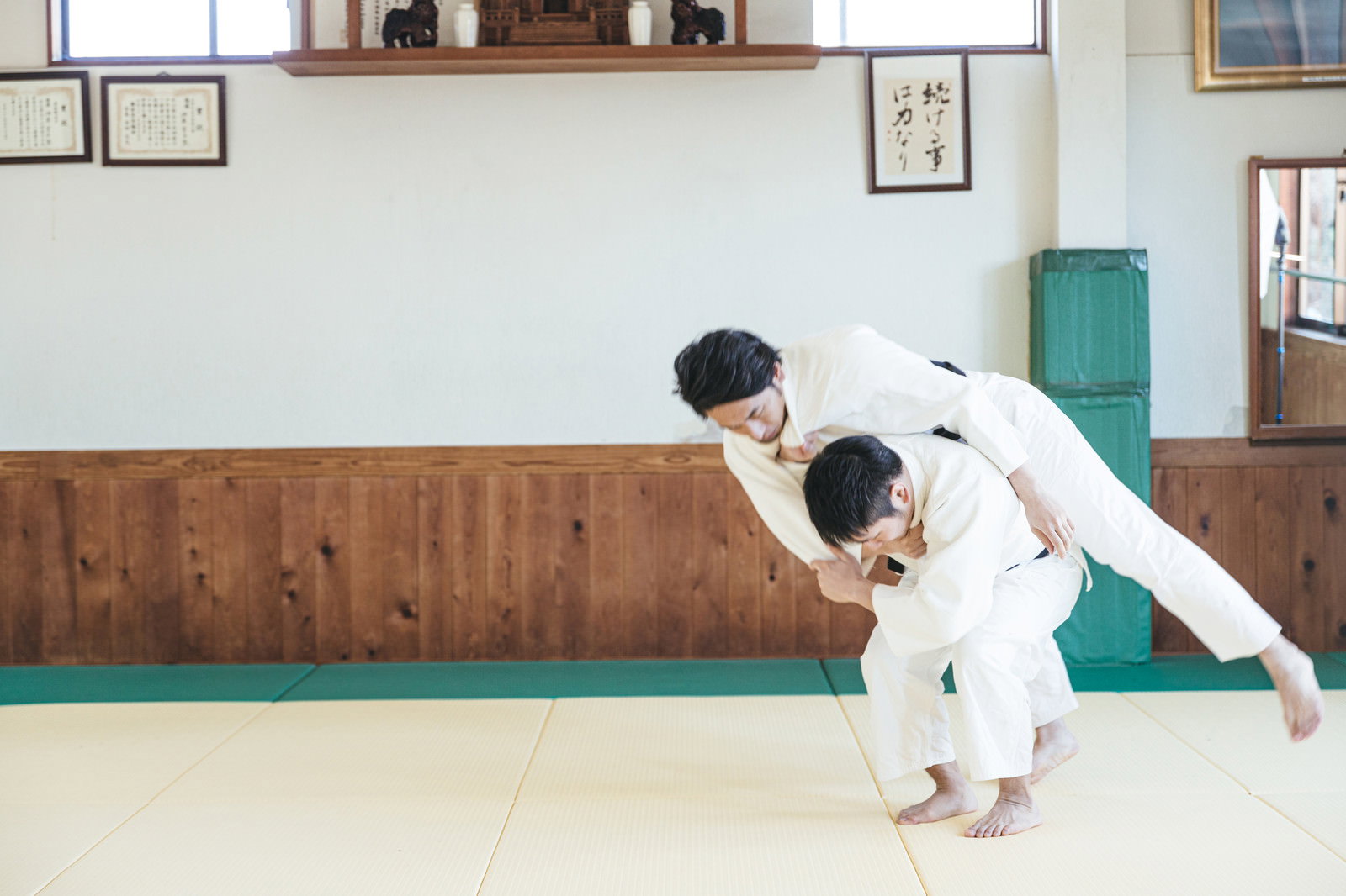 道場の畳の上で白い道着を着た男性が背負投を決めている［モデル：大川竜弥］
