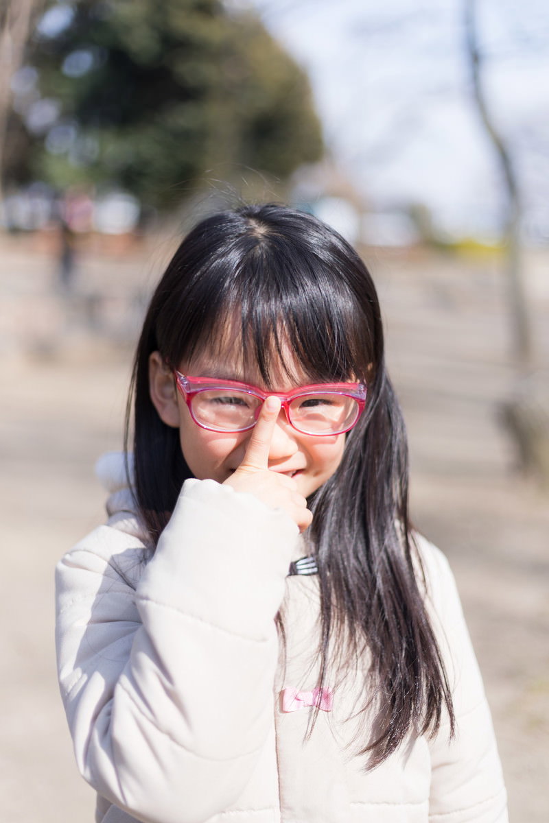 赤いフレームの眼鏡をかけて手を口元に当てて微笑む少女［モデル：あんじゅ］