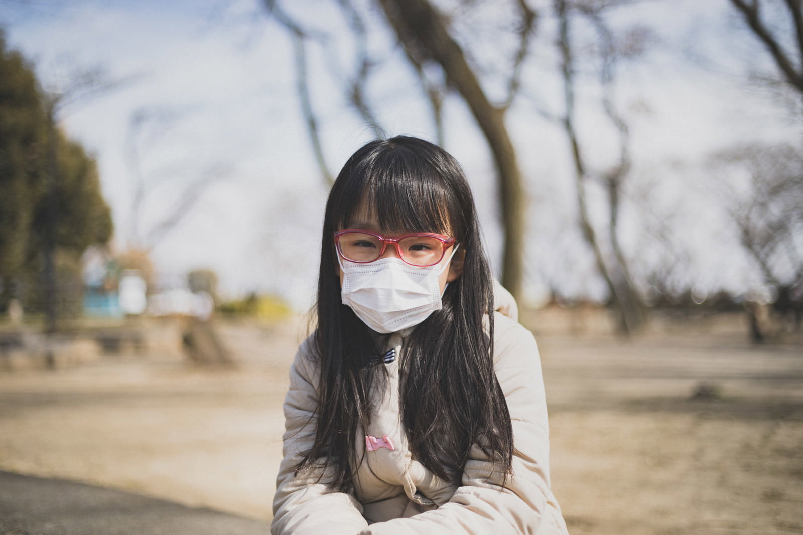 マスクと眼鏡をかけてベンチに座る体調不良の女の子［モデル：あんじゅ］