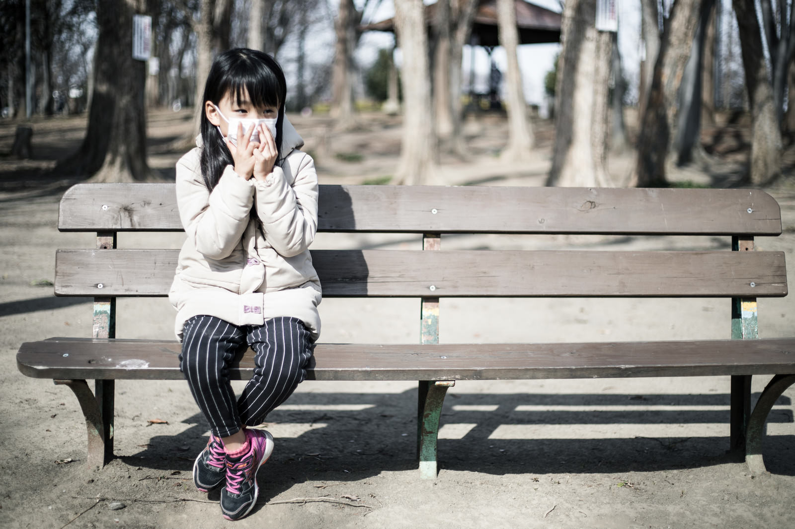 白いマスクを着用してベンチに座り手を頬に当てる女性［モデル：あんじゅ］