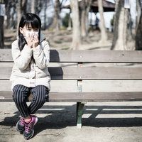 乾燥する季節にマスクを着用して公園のベンチに座る女の子の写真
