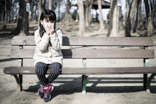 乾燥する季節にマスクを着用して公園のベンチに座る女の子
