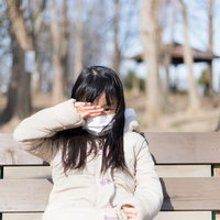 マスクを着用して目が痒くて手でこすってしまう女性の写真