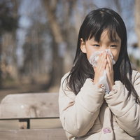 花粉症の時期、ティッシュで鼻をかむ女の子の写真