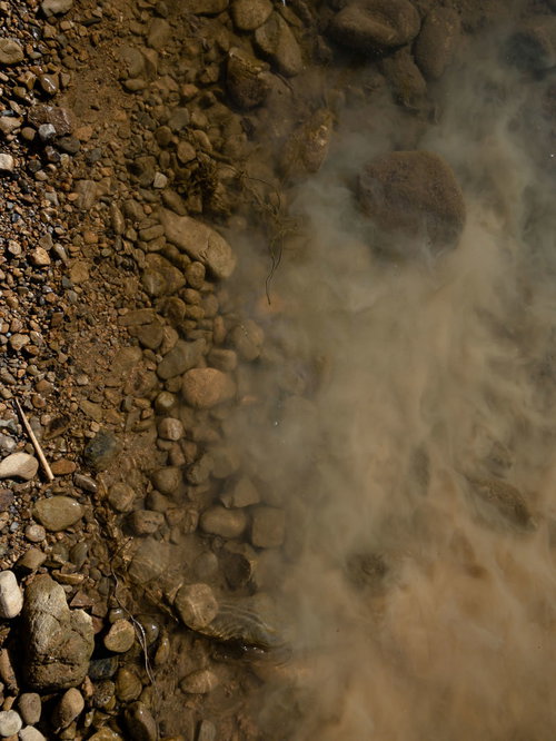 浅瀬の濁った水面のテクスチャー：川底の砂利と泥が舞い上がる自然